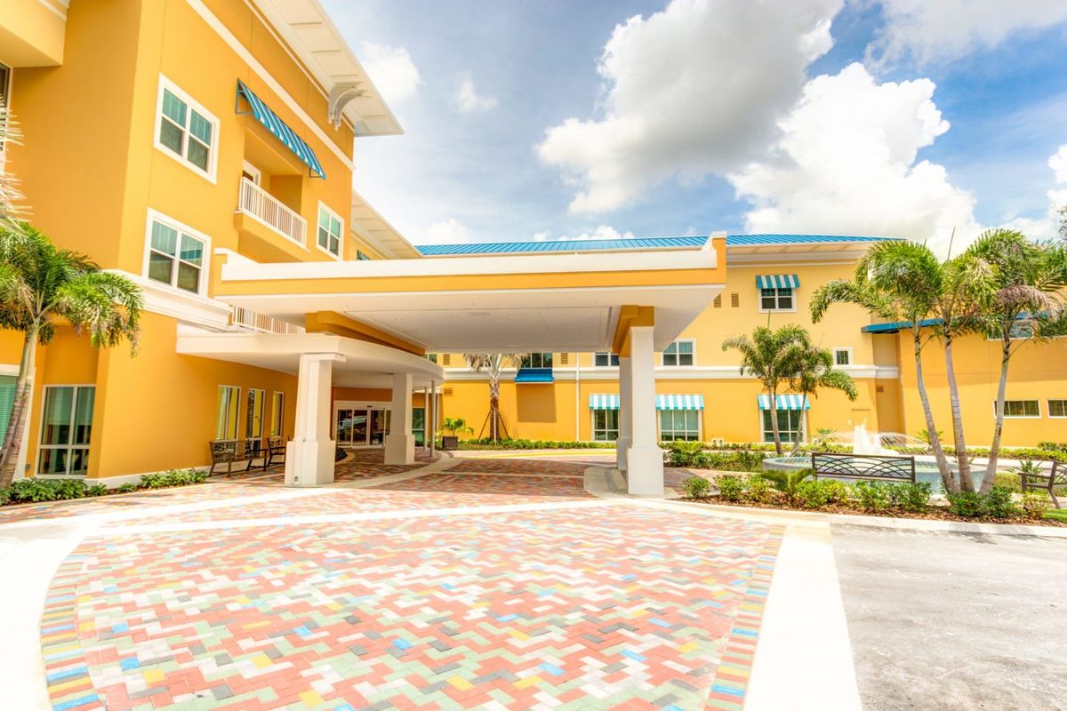 A modern yellow building with a covered entrance and tropical landscaping.
