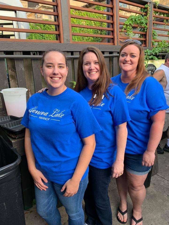 A group of women wearing matching blue shirts, smiling outdoors.