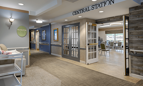 A view of an office hallway with a central station entrance featuring glass doors and a carpeted floor.