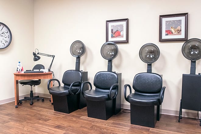 A salon waiting area featuring three hair dryer chairs and framed artwork on the wall.