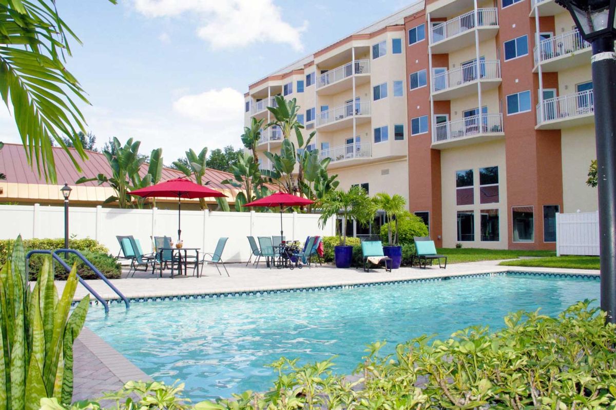 An inviting swimming pool in front of a multi-story apartment building, surrounded by lounge chairs and red umbrellas.