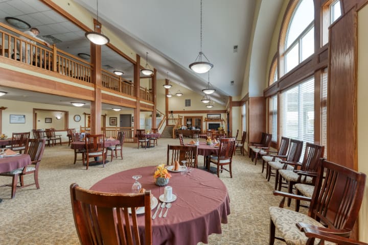 A spacious dining area with elegantly set tables and chairs, featuring large windows and high ceilings with chandeliers.