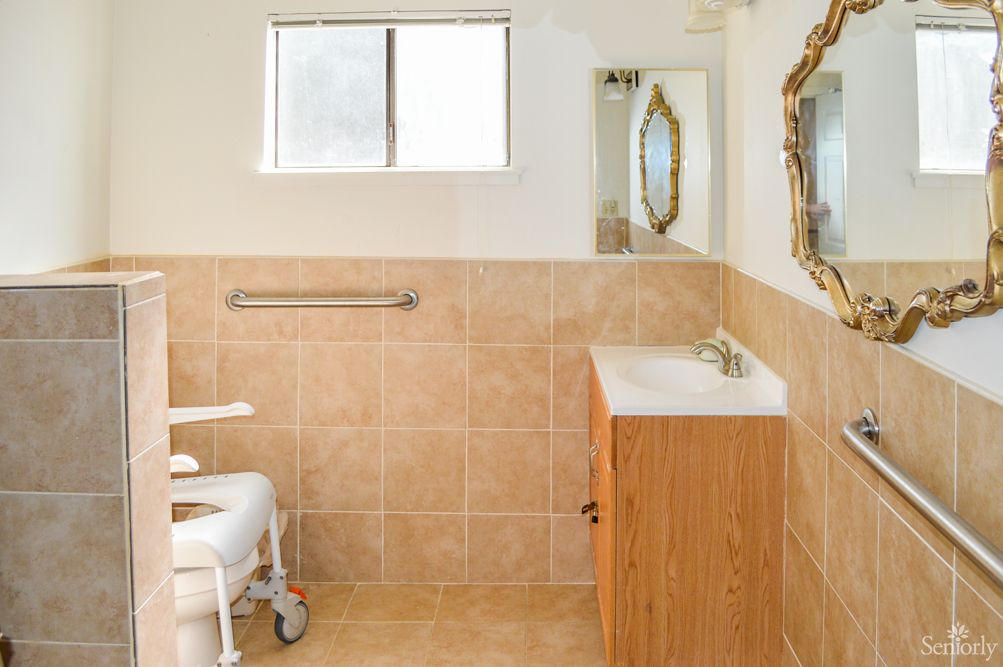 An accessible bathroom with a tiled interior and a wooden vanity.
