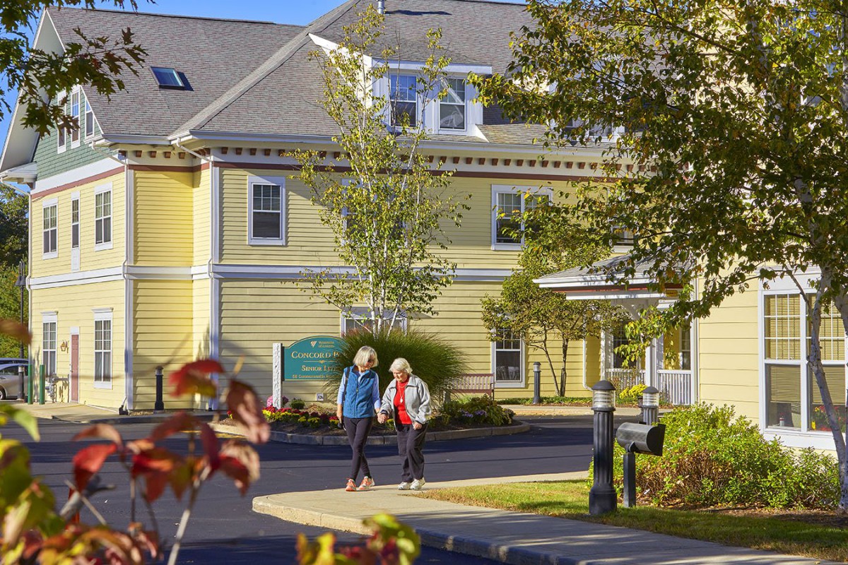 Two seniors walking in front of a yellow building on a sunny day.