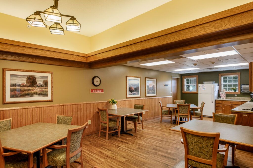 A cozy dining room with wooden floors, tables, and chairs, decorated with wall art and a clock.