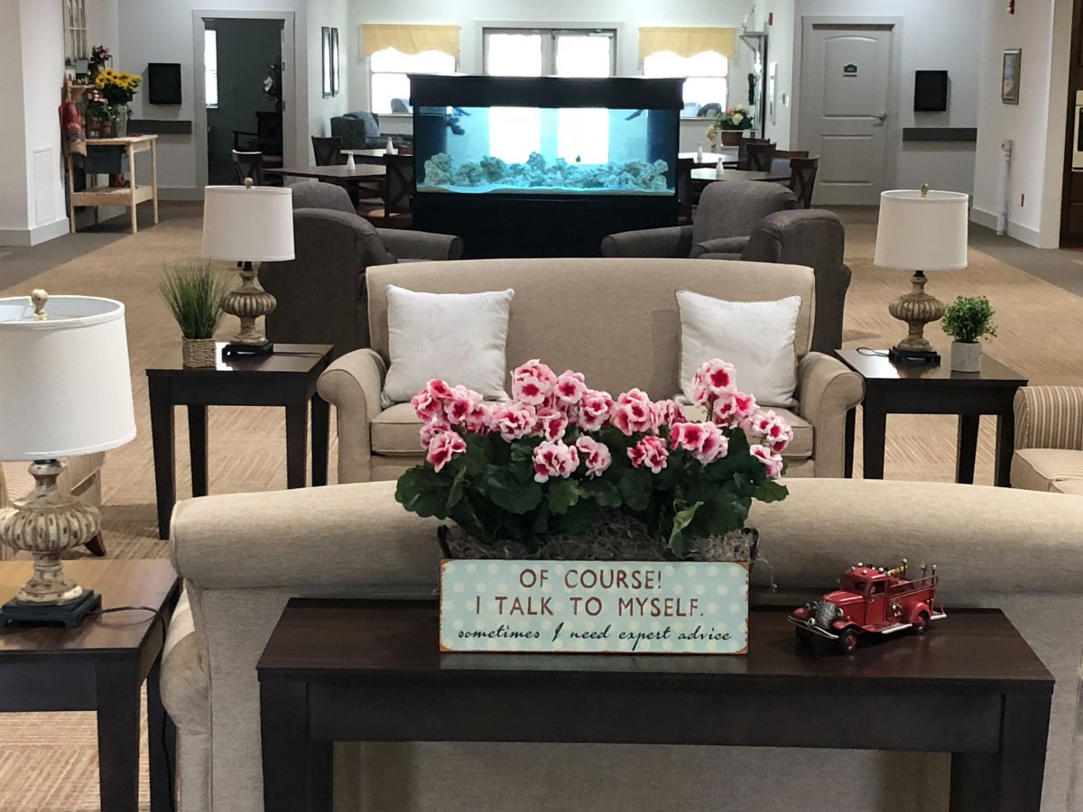 A cozy living room with stylish decor, featuring a floral centerpiece and a humorous sign.