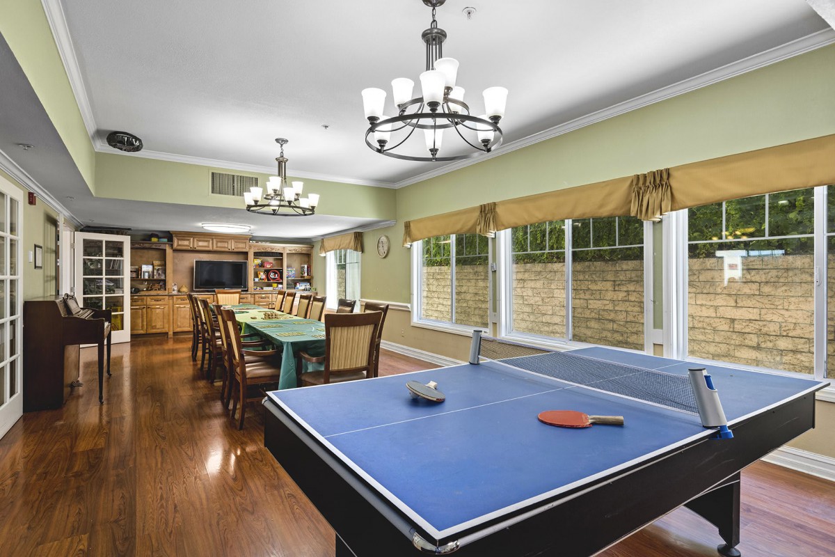 A spacious game room featuring a ping pong table and a dining area with elegant chandeliers.