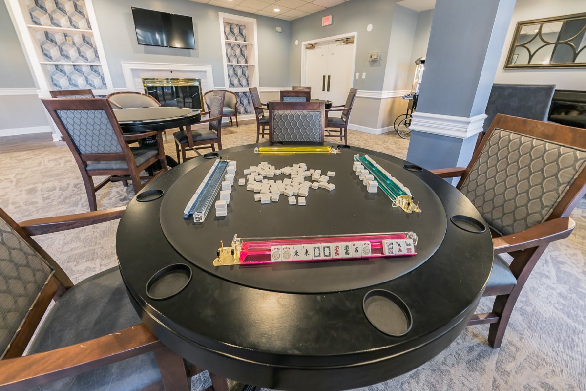 A recreational room featuring a game table set up for Mahjong with chairs arranged around it.