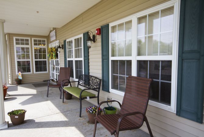 A cozy porch with chairs and a bench, adorned with plants next to large windows.