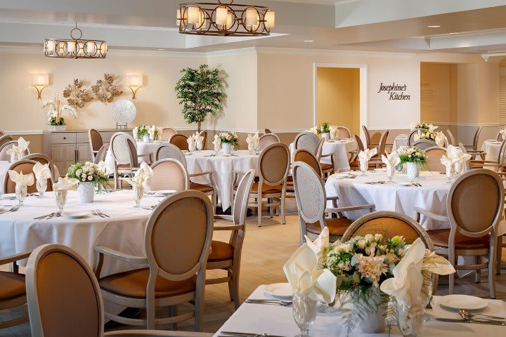 An elegantly set dining room with round tables, chairs, and floral centerpieces.