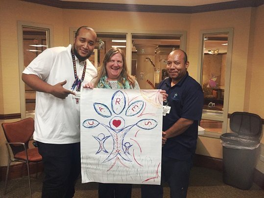 Three people holding a large drawing with a heart and colorful designs.