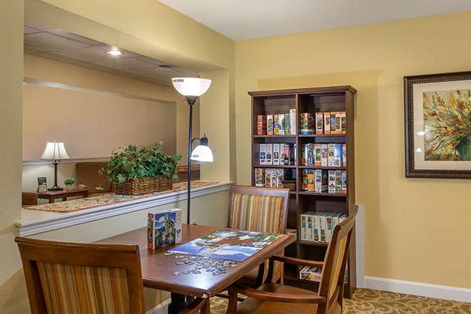 A cozy dining area with a wooden table, chairs, bookshelf, and floor lamp.