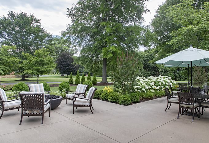 A serene patio setup with outdoor seating surrounded by lush greenery and trees.