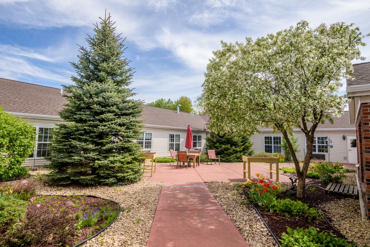 A peaceful garden with a pathway leading to a patio and building, surrounded by trees.