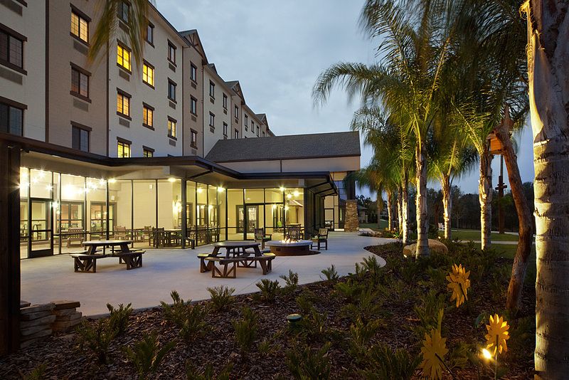 A hotel exterior featuring outdoor seating and palm trees in the evening.