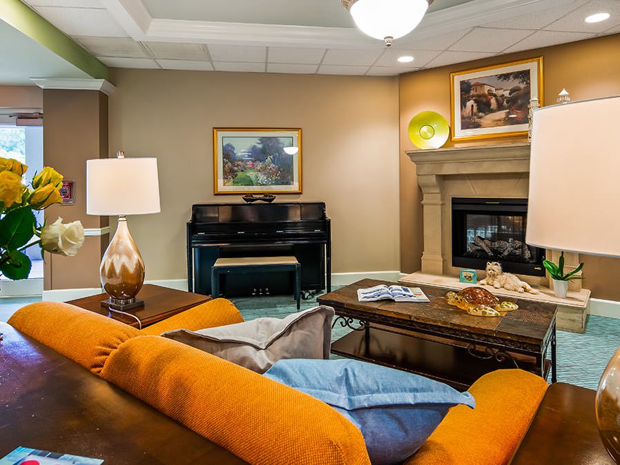 A cozy living room featuring an orange couch, a piano, and a warm fireplace.