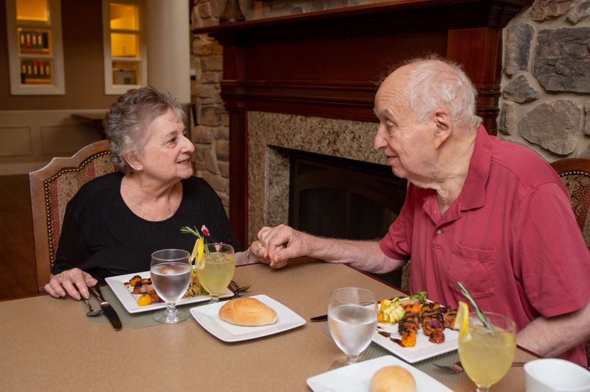 An elderly couple enjoying a meal together while holding hands at a restaurant.