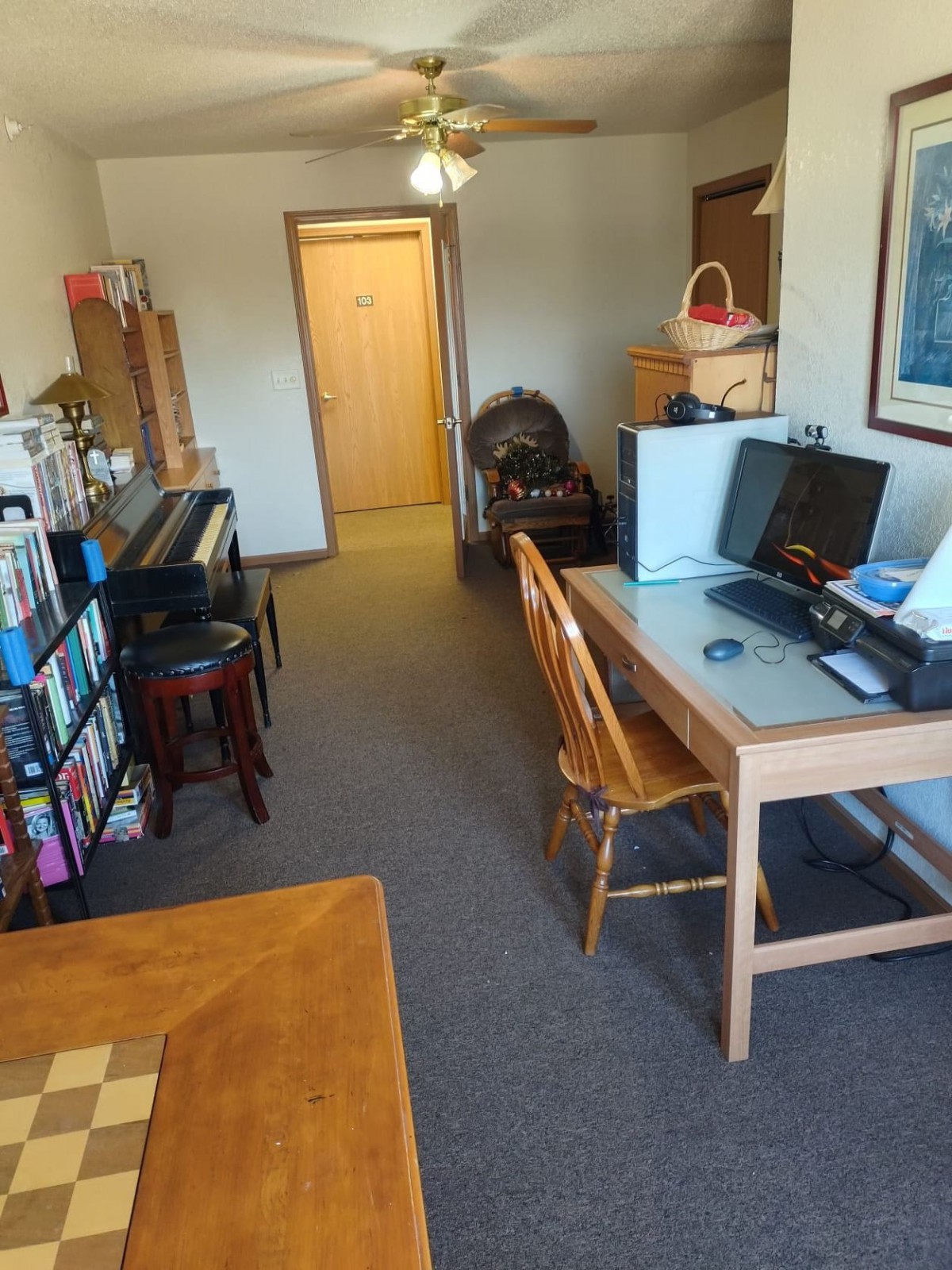 A cozy living room setup featuring a piano, computer desk, and bookshelf.