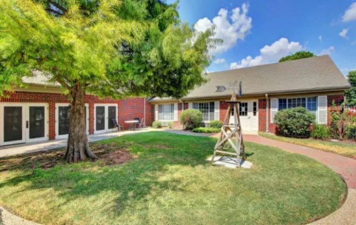A picturesque backyard with a green lawn, a swing, and a brick house under a blue sky with clouds.