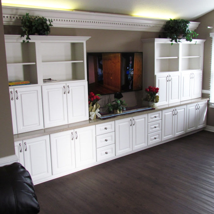 A stylish white entertainment center with open shelving and closed cabinets, adorned with decorative plants, in a well-lit living room.