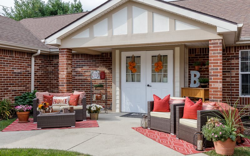 A cozy front porch with wicker furniture and red accents, perfect for relaxing outdoors.