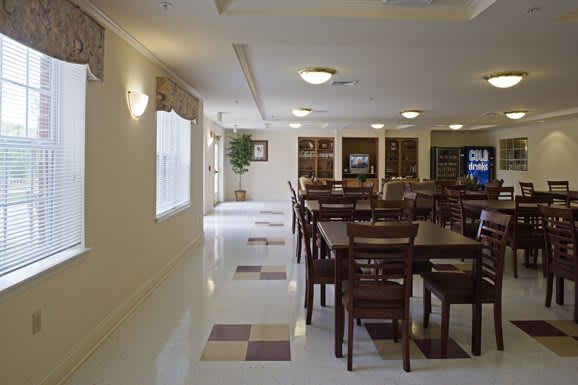 A spacious dining area with multiple tables and chairs, well-lit by ceiling lights and natural light from the windows.
