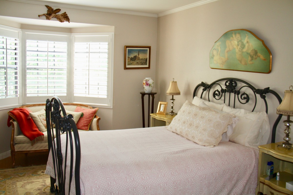 A cozy bedroom with a wrought-iron bed, well-lit by natural light from the window.
