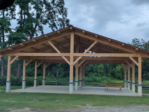 A spacious wooden pavilion located in a lush green park, offering shelter and a place to relax amidst nature.