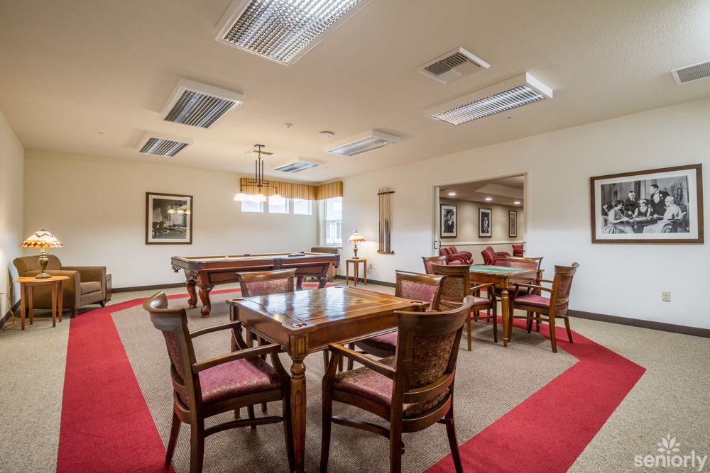 A spacious game room featuring a billiards table, multiple chairs and tables, with ample lighting.