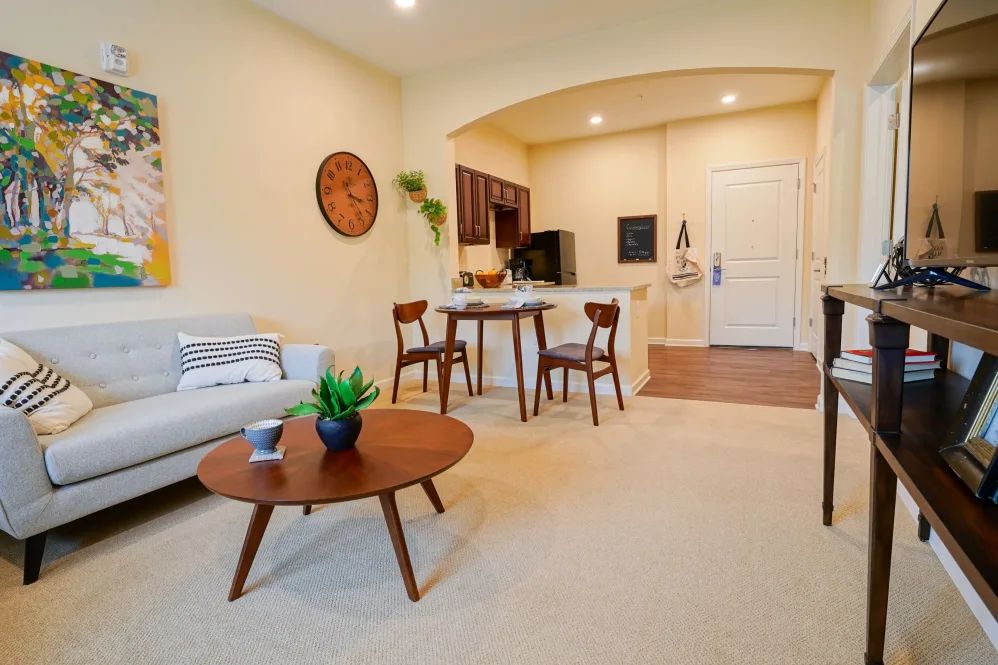 A modern open-concept apartment interior featuring a cozy living room with a sofa and coffee table, adjacent to a small dining area and kitchen.