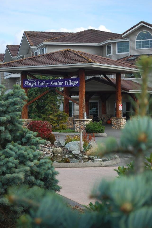 A building entrance with a landscape featuring trees and a visible sign above.