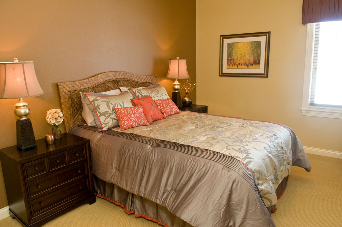 A cozy bedroom with a neatly made bed, decorative pillows, and a warm lamp on the nightstand.
