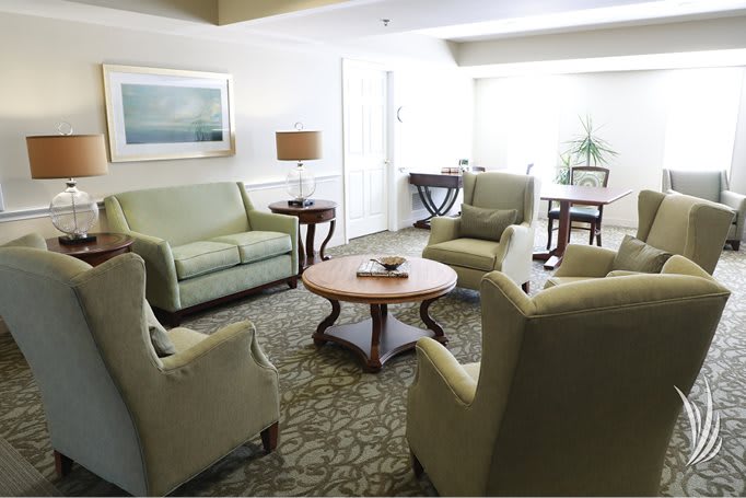 A cozy living room with green sofas, armchairs, and a round wooden coffee table.