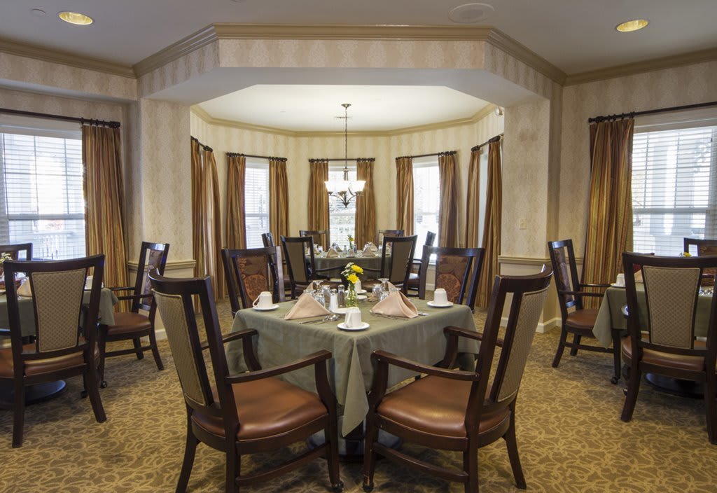 An elegantly designed dining room with a round table set for a meal, surrounded by high-backed chairs and illuminated by a chandelier.