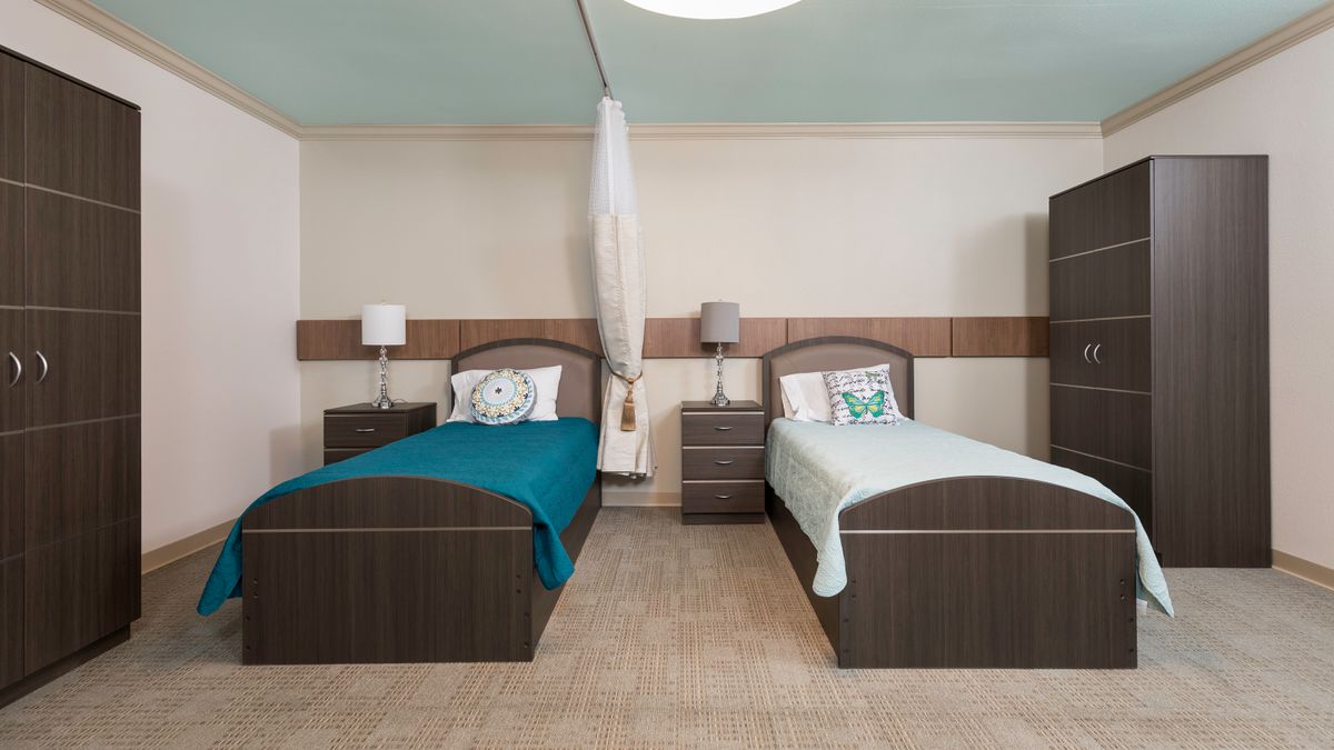 A modern bedroom featuring two single beds with colorful linens, complemented by bedside lamps and a central nightstand.