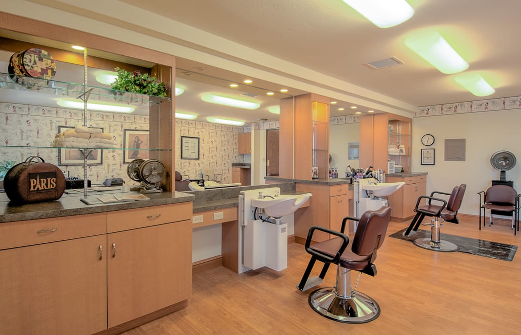 An empty hair salon with chairs and mirrors lined up along a counter.