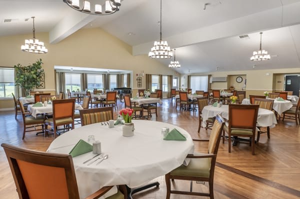 A spacious and elegantly furnished dining room with neatly arranged tables and chairs, featuring chandeliers.
