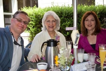 A group of three people smiling during an outdoor brunch.