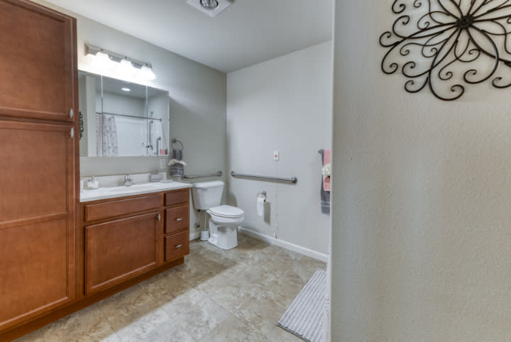 A clean and modern bathroom with a wooden cabinet, sink, toilet, and mirror.