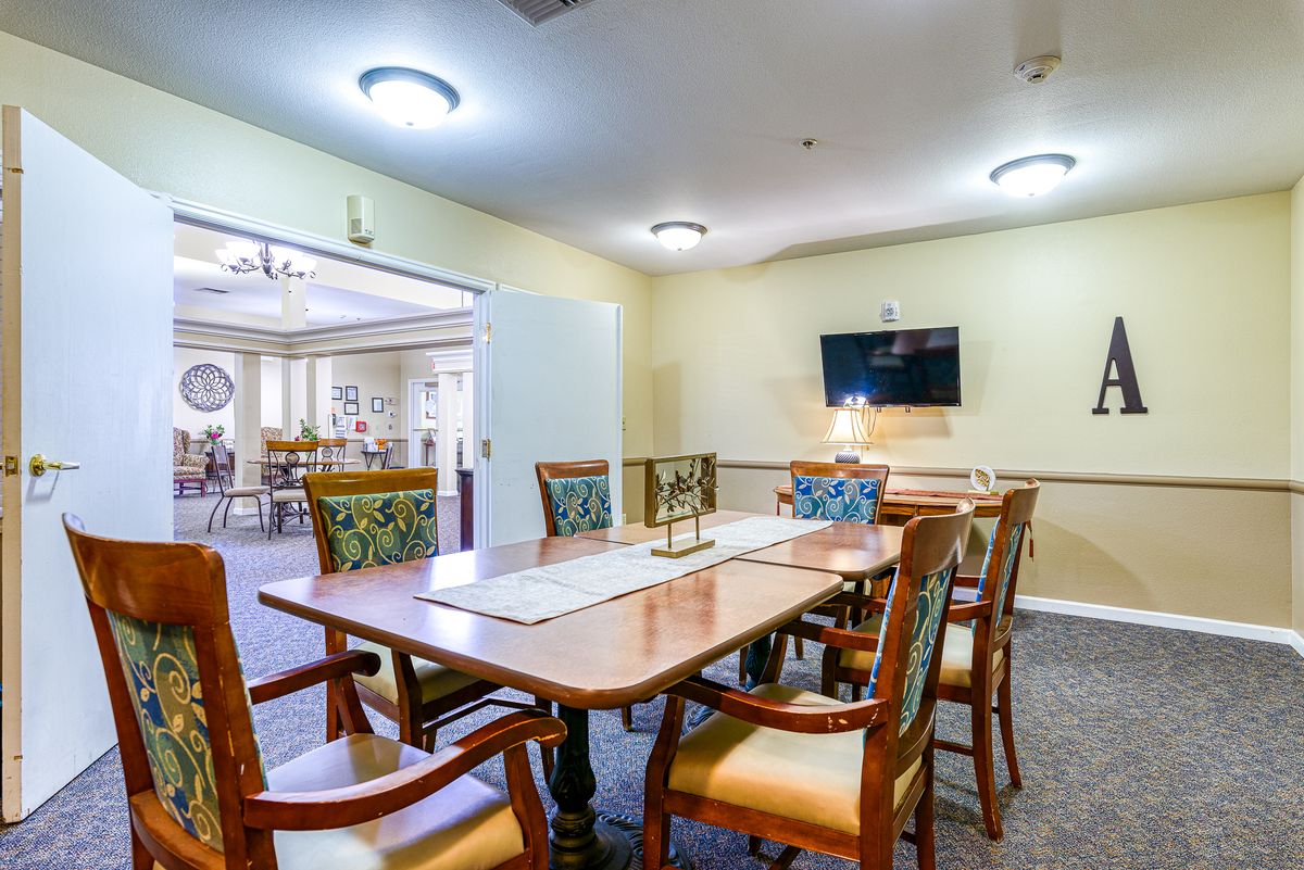 A well-lit dining room with a large table, chairs, and a wall-mounted television.