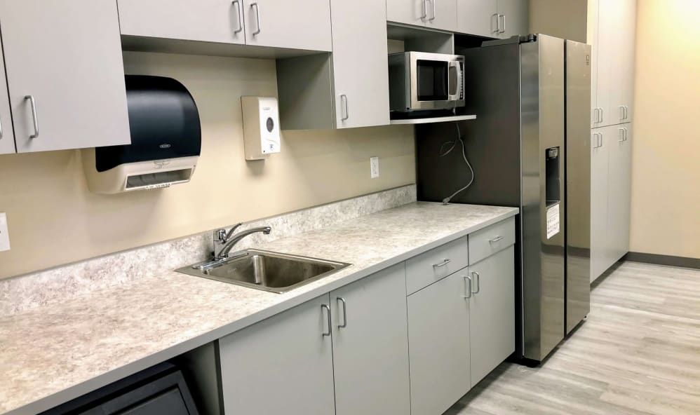 A modern office kitchen with a sink, microwave, and stainless steel refrigerator.