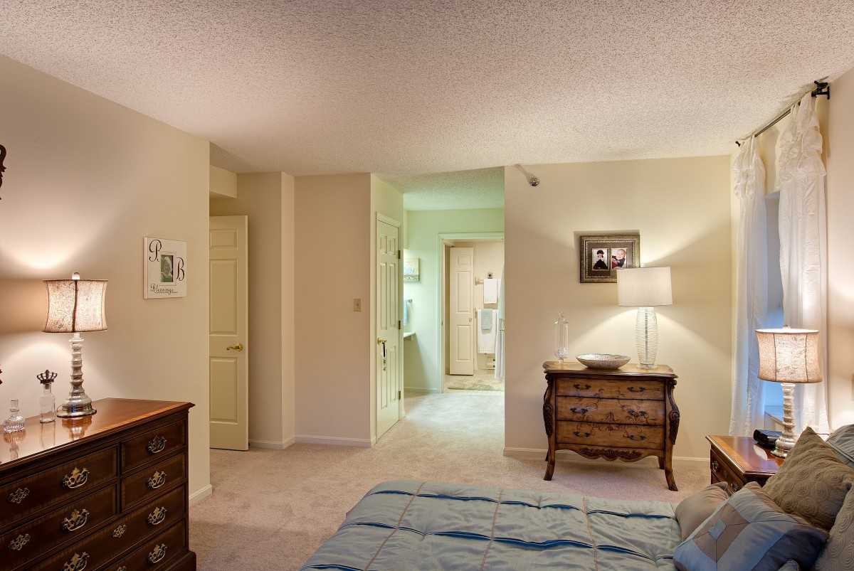 A cozy bedroom with a lamp and dresser, leading into an adjoining room.