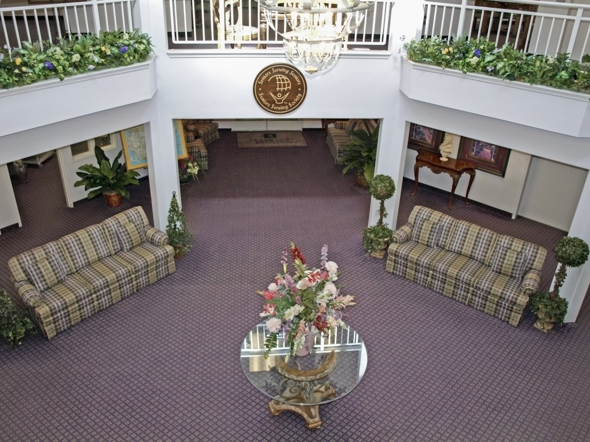 A spacious lobby featuring elegant furniture, a central floral arrangement, and a chandelier hanging from above.