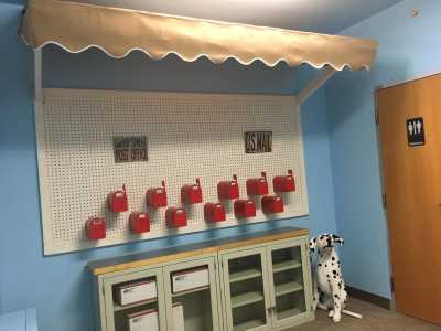 A children's playroom featuring interactive red mailboxes on a blue wall, with a Dalmatian statue and wooden cabinets.