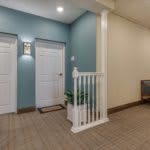 A well-lit hallway with two white doors and a small staircase leading to a landing area, featuring blue and beige walls.