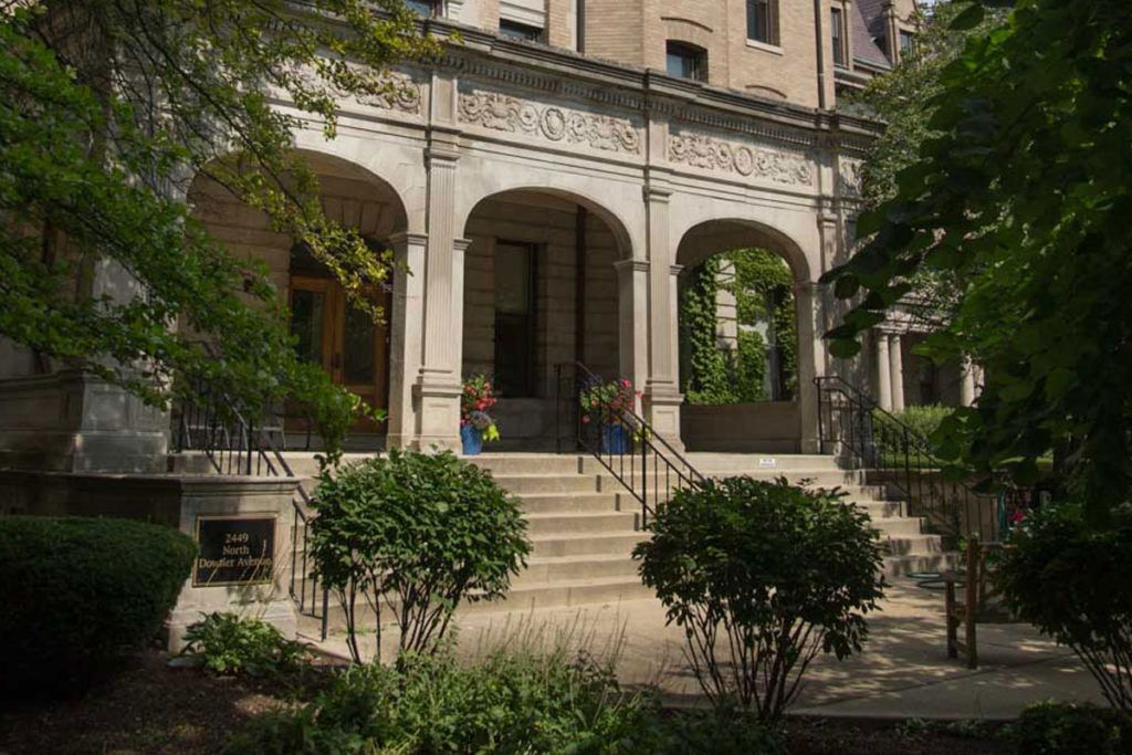 A historic building entrance with arched windows and lush greenery.