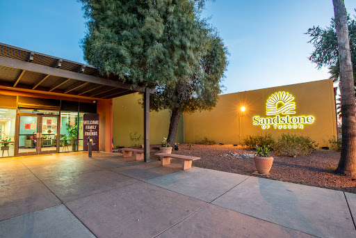 Entrance to a building illuminated in the evening, surrounded by landscaping.