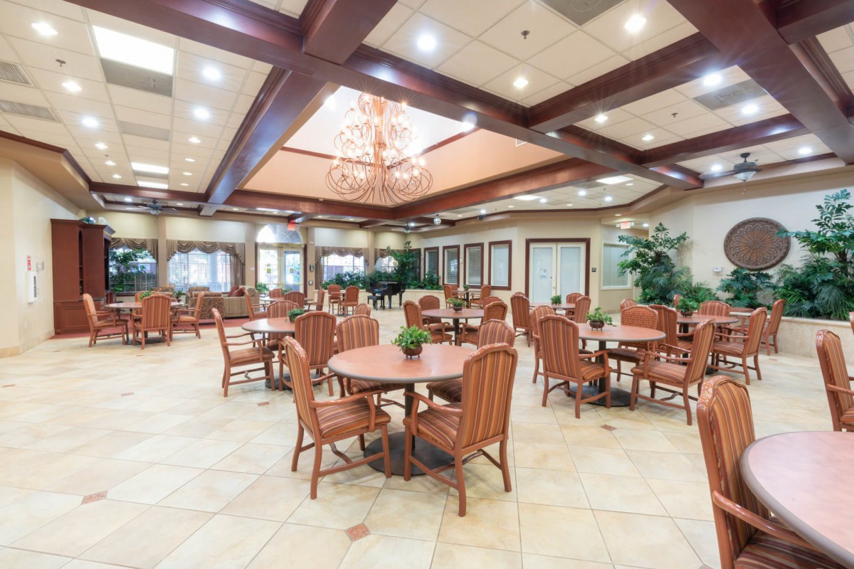 A spacious dining area with wooden tables and chairs, featuring a chandelier and decorative wood beams.