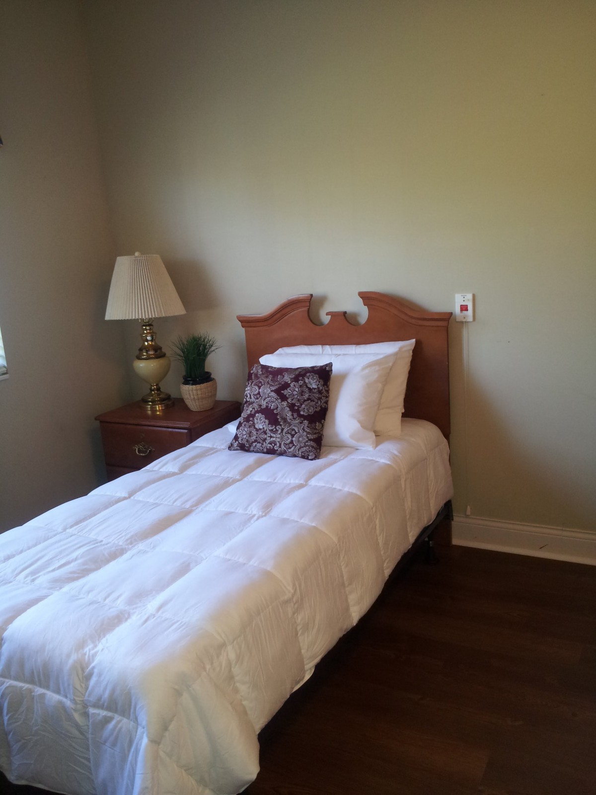 A cozy bedroom with a neatly made single bed and a nightstand with a lamp.