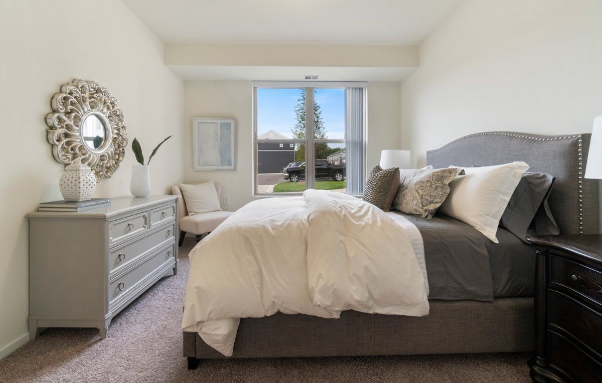 A modern bedroom featuring a comfortable bed with neutral-colored bedding, complemented by stylish furniture and a large window offering an outdoor view.